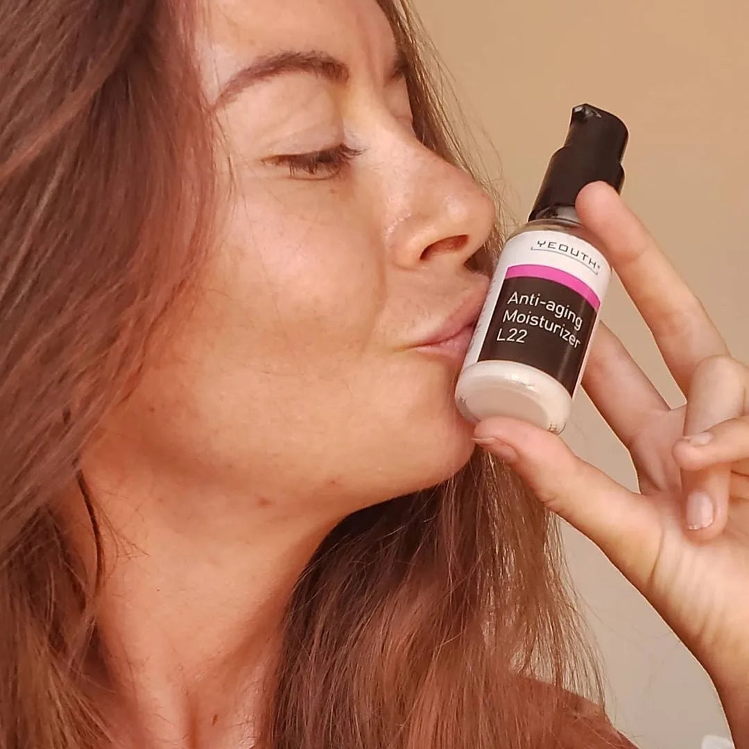 A woman smiling while holding and kissing a YEOUTH Anti-Aging Moisturizer L22 bottle close to her face.