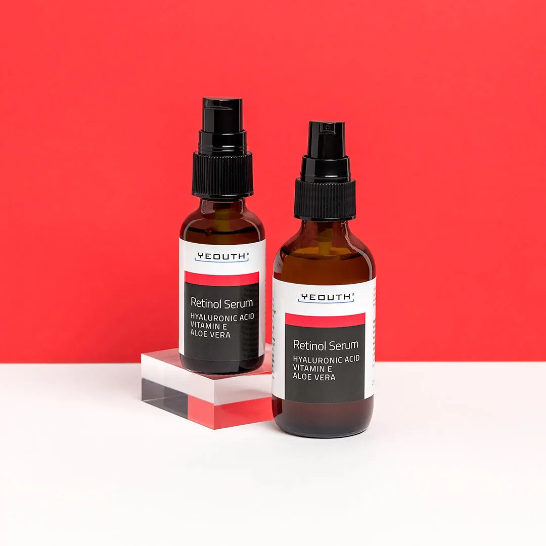 Two bottles of YEOUTH Retinol Serum with Hyaluronic Acid, Vitamin E, and Aloe Vera against a red background.