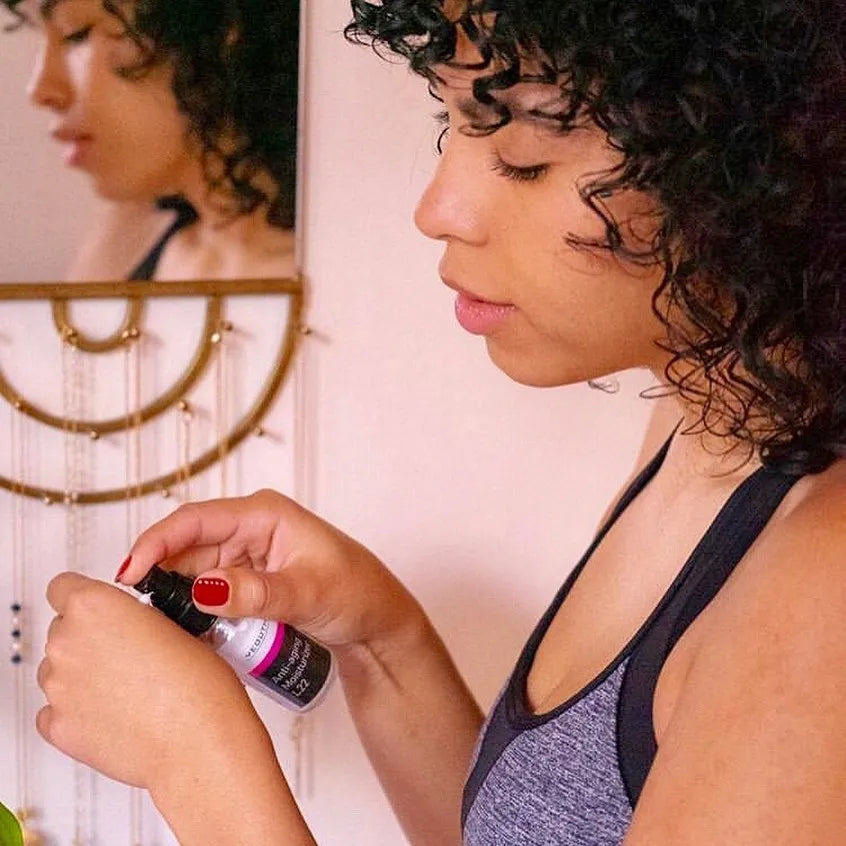 A woman applying YEOUTH Anti-Aging Moisturizer L22 while standing near a mirror, wearing a tank top.