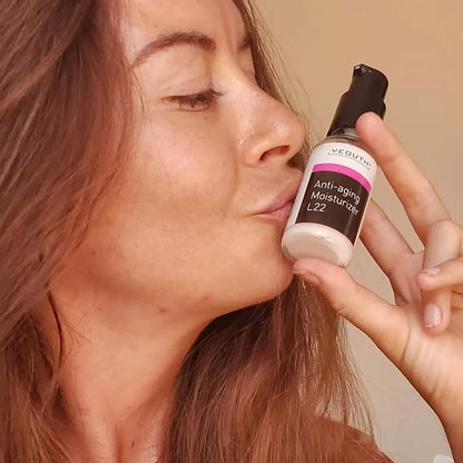 A woman smiling while holding and kissing a YEOUTH Anti-Aging Moisturizer L22 bottle close to her face.