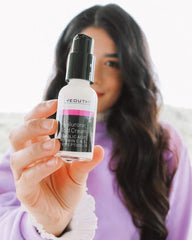 Woman in a lavender sweater holding a bottle of YEOUTH hyaluronic acid lotion with focus on the product label.