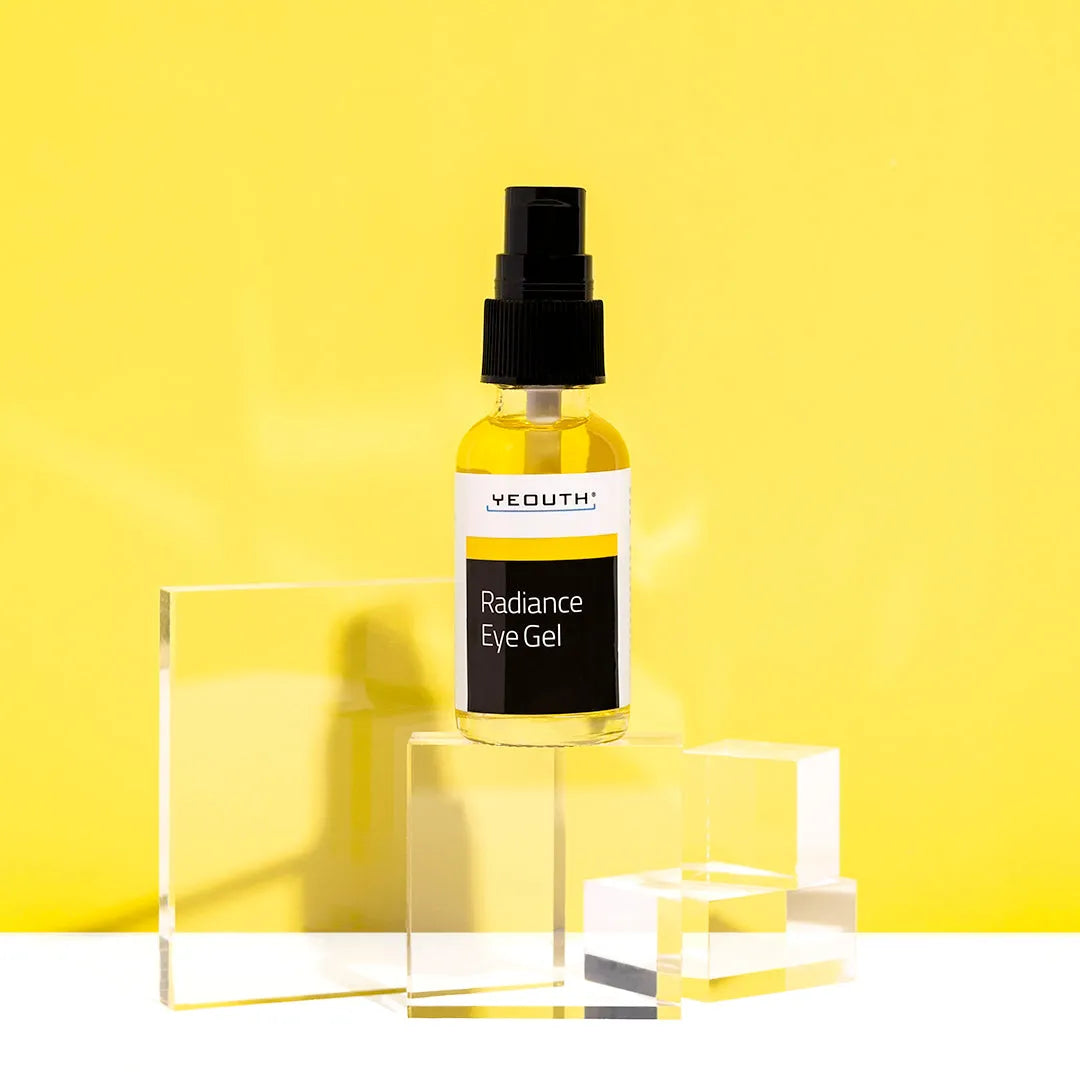YEOUTH Radiance Eye Gel bottle on clear acrylic blocks with bright yellow background, clean skincare product photo.