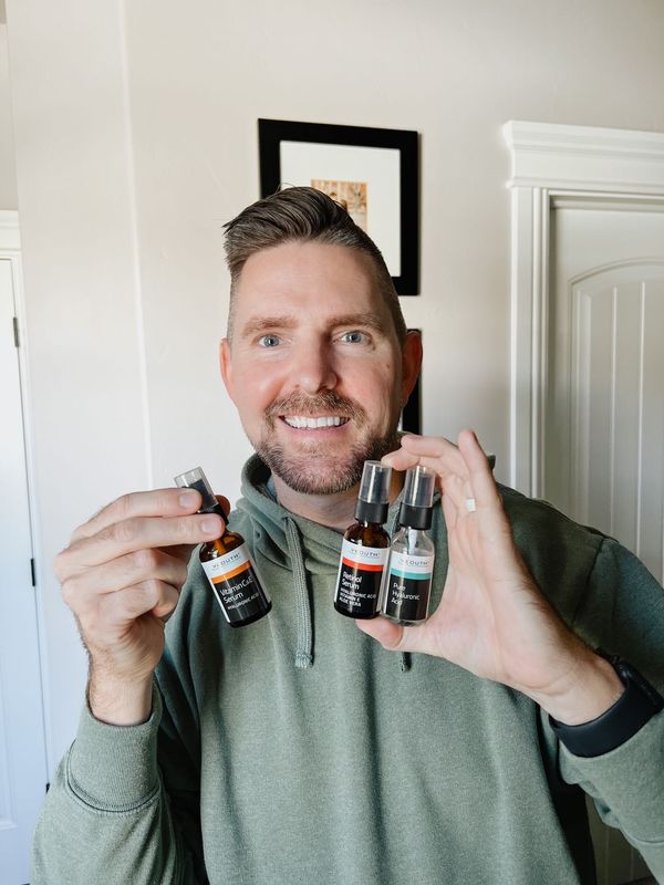 Man smiling while holding three YEOUTH skincare serums: Vitamin C&E Serum, Retinol Serum, and Pure Hyaluronic Acid.