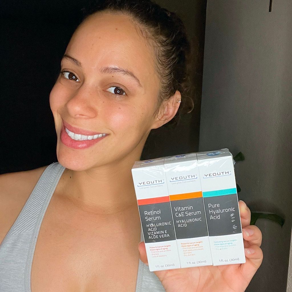 Woman smiling and holding three YEOUTH skincare serums: Retinol Serum, Vitamin C&E Serum, and Pure Hyaluronic Acid.